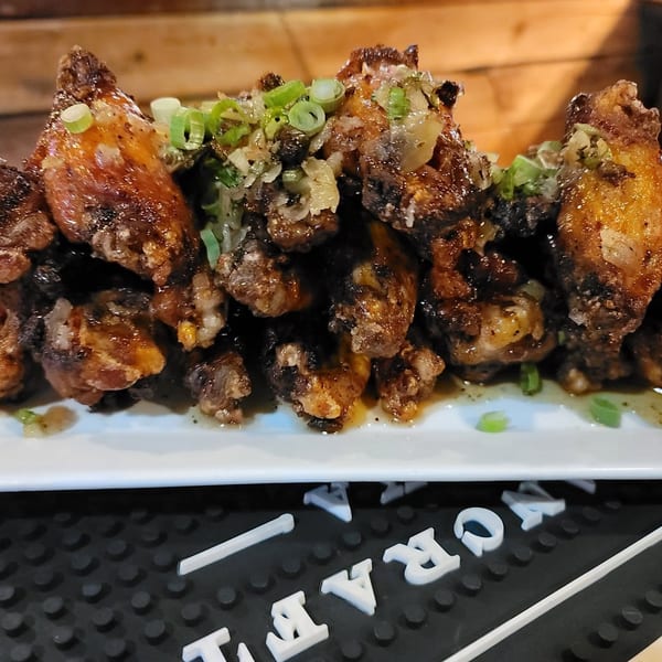 Crispy fried chicken wings topped with chopped green onions and garlic on a white rectangular plate.