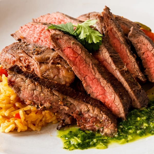 Sliced medium-rare steak with yellow rice, green sauce, and cilantro on a white plate.