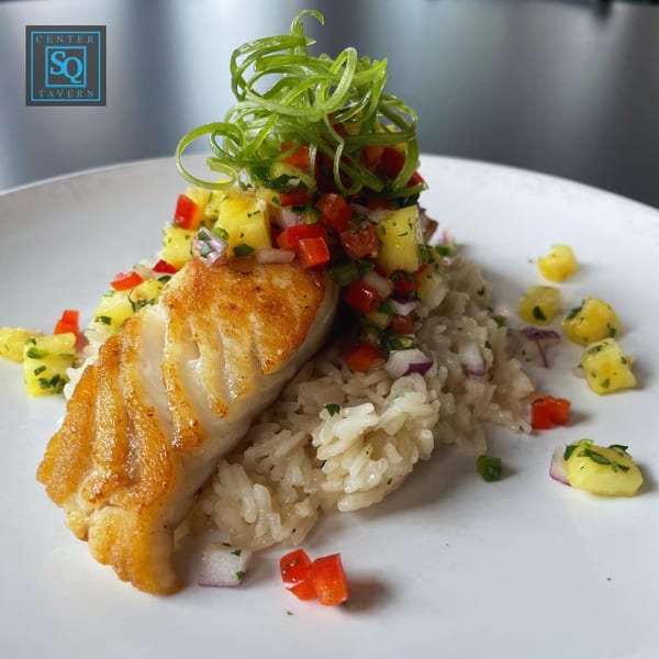 Pan-seared fish with rice, pineapple salsa, and green onion garnish on a white plate.