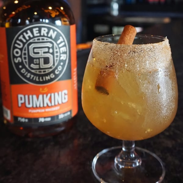A Southern Tier Pumking whiskey bottle next to a cocktail with a sugar rim and cinnamon stick.
