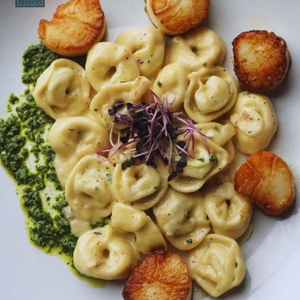 Tortellini pasta with seared scallops, pesto, and microgreens on a white plate.