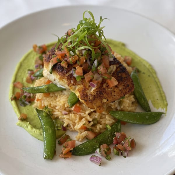 Pan-seared fish with salsa, green onions, snap peas, and rice on a bed of green sauce.