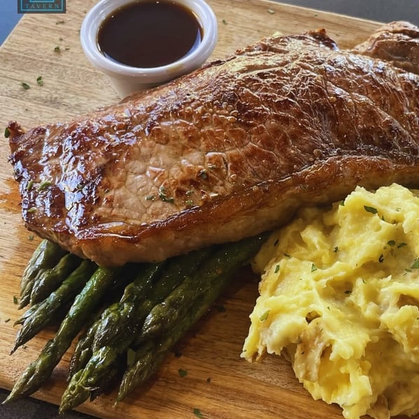 Center Square Tavern's steak, mashed potatoes, asparagus, and gravy on a wooden board.