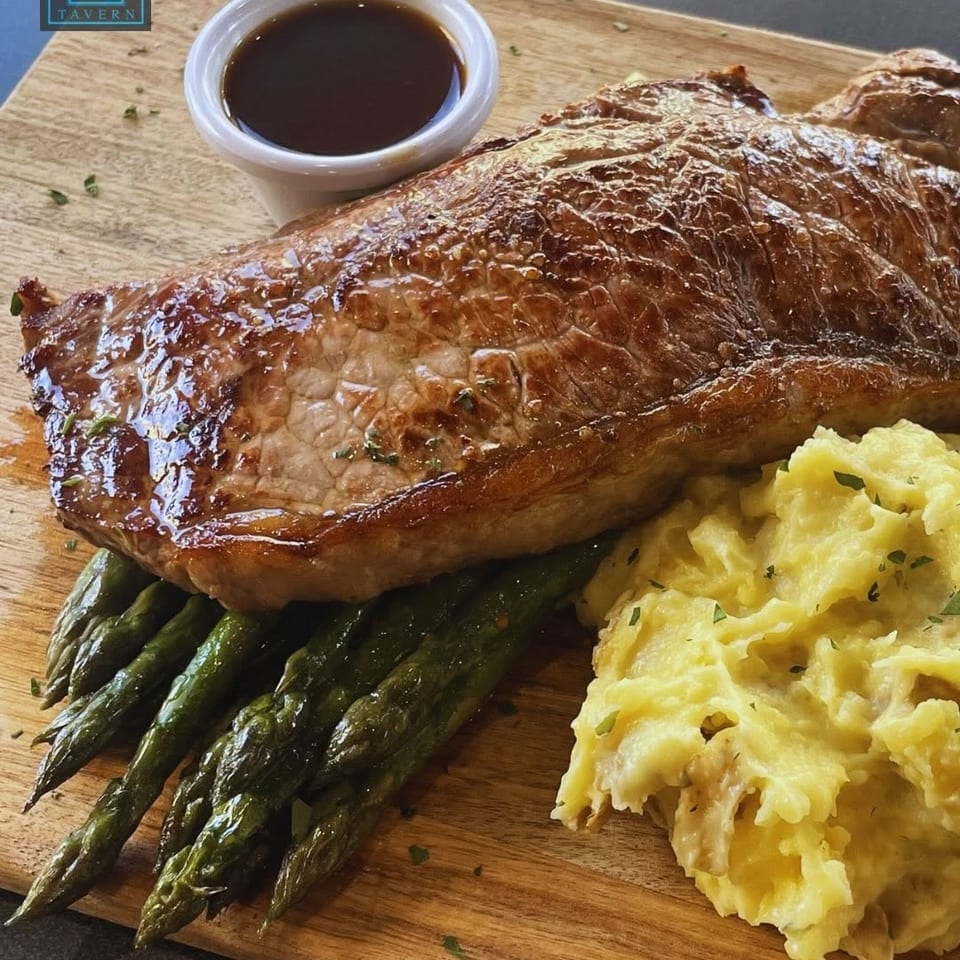 Center Square Tavern's steak, mashed potatoes, asparagus, and gravy on a wooden board.