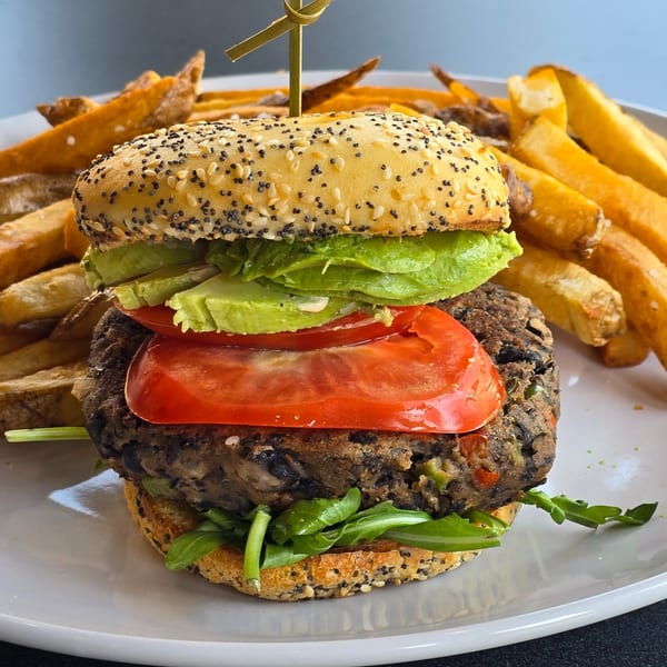 A veggie burger with avocado, tomato, and arugula, served with a side of fries.