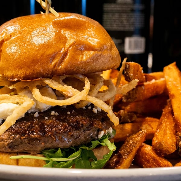 Gourmet burger with goat cheese, crispy onion rings, arugula, and sweet potato fries.