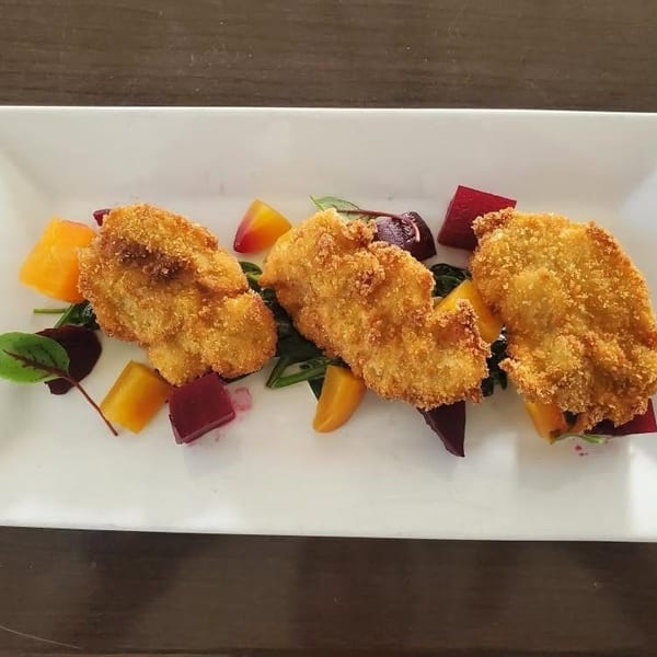 Three breaded chicken cutlets on a bed of greens with diced orange and red beets.
