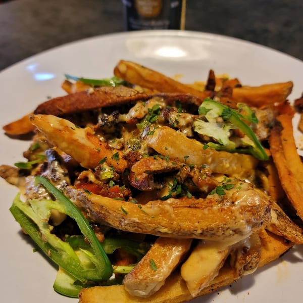 Loaded fries with cheese, meat, jalapeños, and parsley, with a Corona Extra bottle in the background.